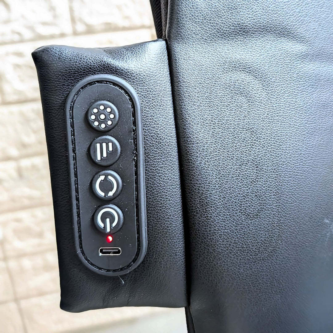 Close-up of a black textured leather or faux-leather control panel with four buttons and a USB-C port, attached to a black padded item against a light stone wall background.