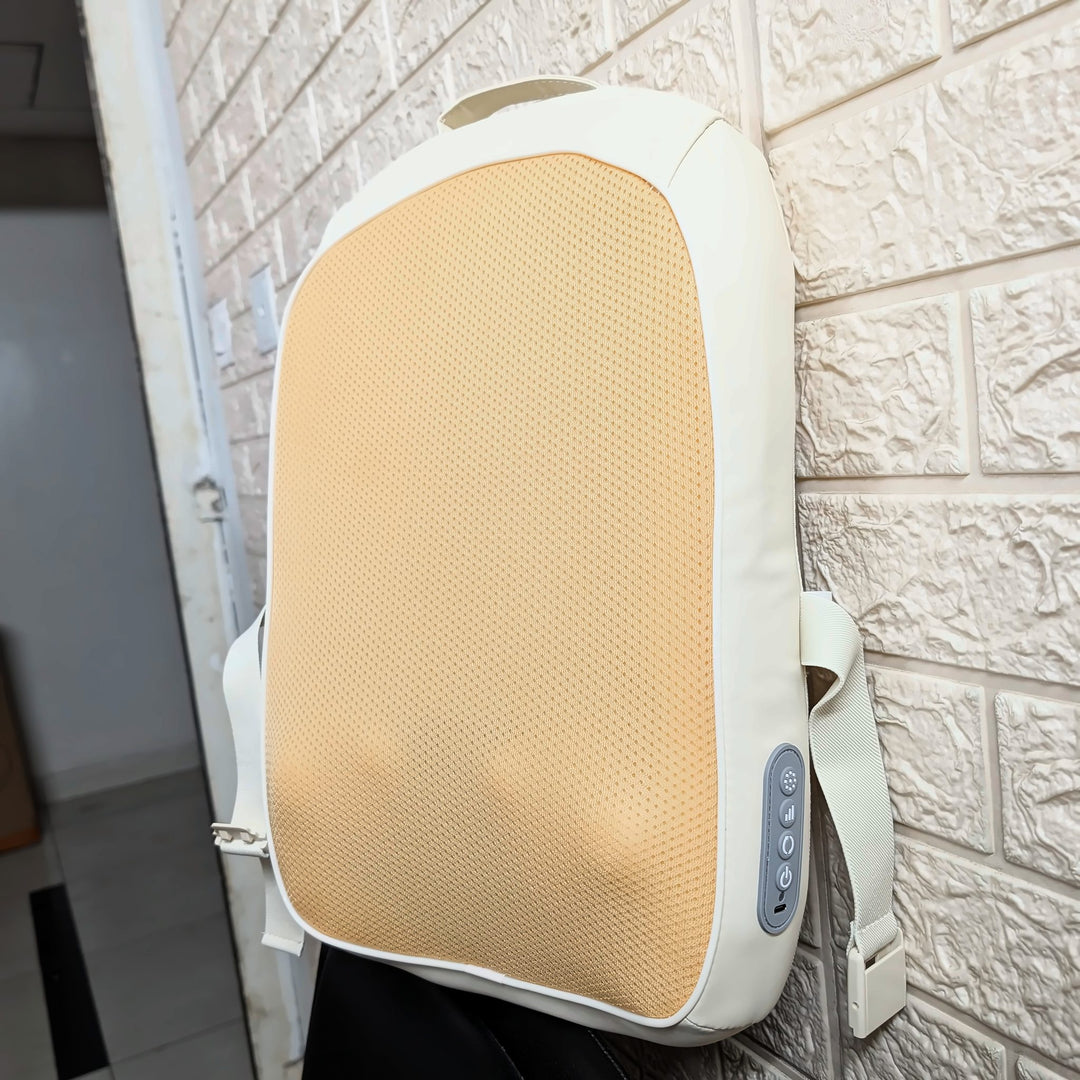 A white and beige electric back massage bag with a textured mesh panel, leaning against a white brick wall.
