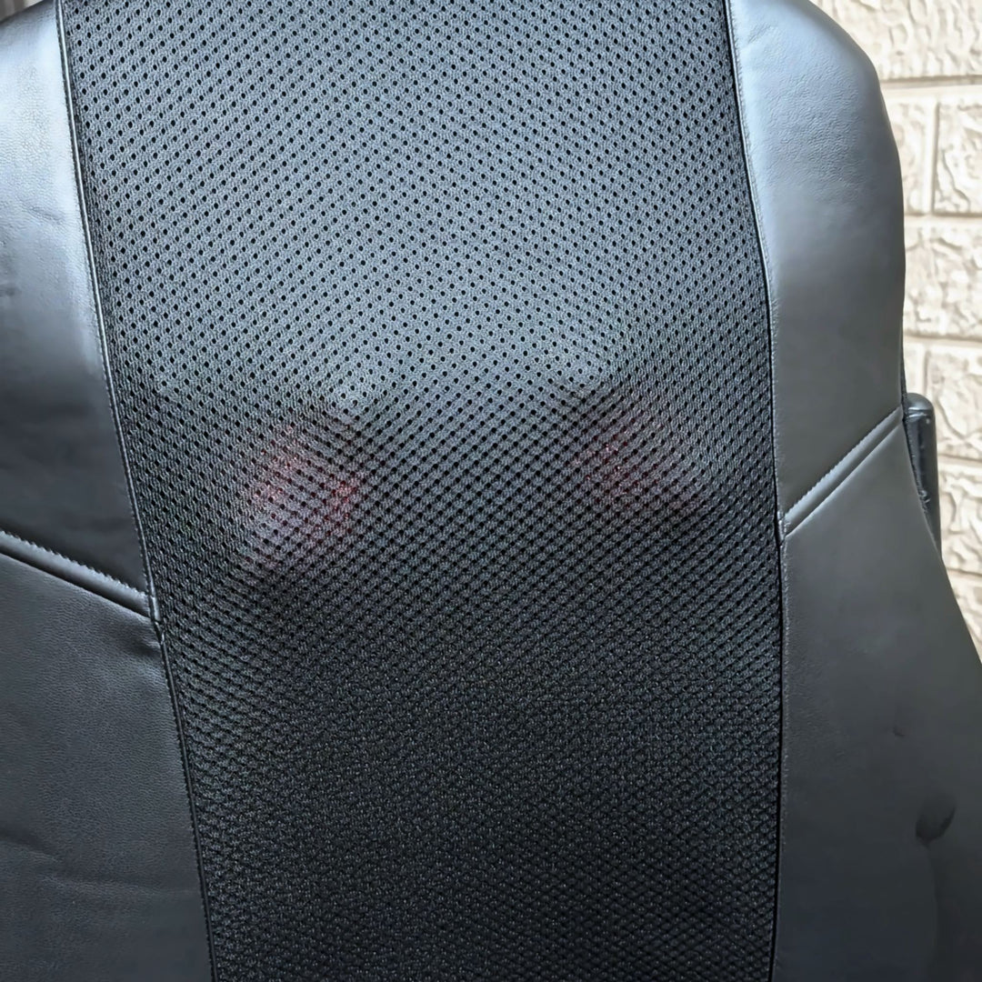 Close-up of a black mesh backrest panel on an office chair, with black faux-leather side panels and a light textured wall in the background.